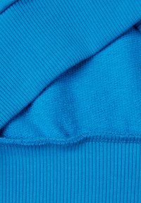 Jasně modrá látka s texturovanými a hladkými sekcemi; okraje mají žebrovaný vzor a uvnitř měkkou, nadýchanou vrstvu.