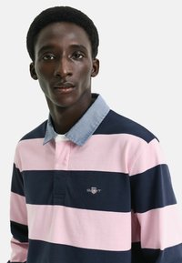 Polo con righe orizzontali blu navy e rosa, colletto in denim e logo ricamato sul petto. Tessuto in cotone, vestibilità casual, maniche lunghe.