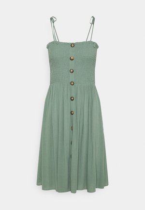 Vestido de verano verde salvia con tirantes finos, corsé fruncido y botones marrones que bajan por el centro delantero hasta una falda midi fluida.