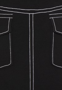 Schwarzer Stoff mit weißen Nähten, ausgestattet mit zwei oberen Taschen und vertikalen Linien, die ein strukturiertes Aussehen präsentieren.