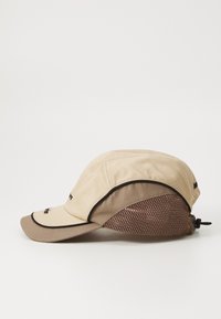 Casquette beige avec un panneau en maille marron, visière incurvée et sangle réglable. Présente un bord contrastant et un branding minimal.
