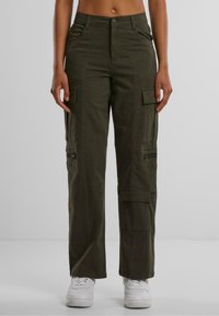 Pantaloni cargo in cotone verde scuro, con tasche laterali, chiusura frontale con zip e vestibilità comoda. Abbinati a sneakers bianche.
