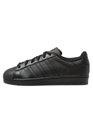 Zapatilla negra de corte bajo con puntera texturizada, tres franjas laterales, cordones y la marca "Superstar" en el lateral.