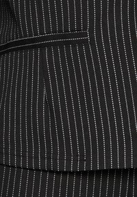 Czarna tkanina z białymi prążkami. Charakteryzuje się eleganckim fasonem, gładką teksturą i kieszenią. Szwy są starannie wykończone.