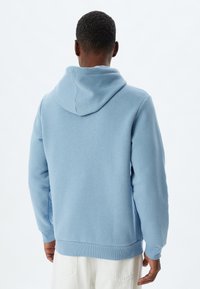 Sudadera azul claro hecha de tela suave, con una gran capucha, puños y dobladillo acanalados, diseño relajado y minimalista.