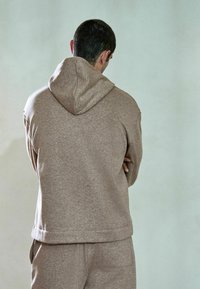 Brun hættetrøje i tekstureret stof med snøre i hætten og kængurulomme, kombineret med matchende joggingbukser.