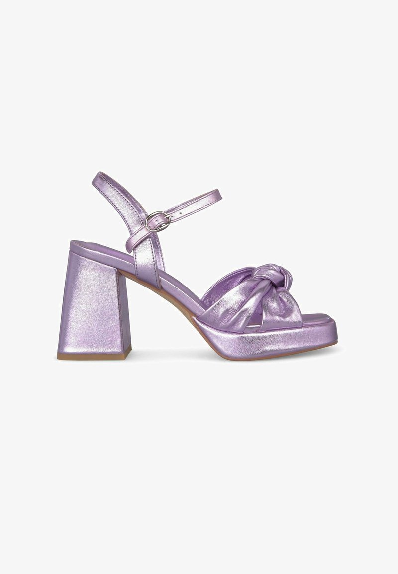 Sandalias metálicas moradas con tacón bloque y tiras al tobillo, con un detalle frontal anudado. Textura suave y un tacón ancho y grueso.
