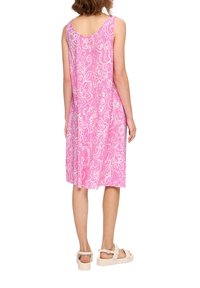 Rosa ärmelloses Kleid mit weißen Blumenmustern, knielang und mit weichem Stoff. Kombiniert mit hellen, klobigen Sandalen.