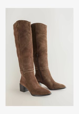 Braune Wildlederstiefel bis zum Knie mit spitzem Schuh und Blockabsatz. Merkmale sind silberne Nieten entlang der Oberkante und einer horizontalen Naht. Mit seitlichem Reißverschluss.