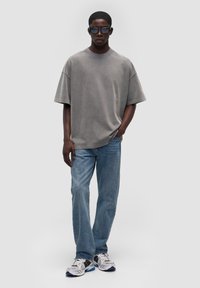 Oversize szary T-shirt z bawełny, proste niebieskie dżinsy i czarno-białe trampki. Cechy: luźny krój i krótkie rękawy.