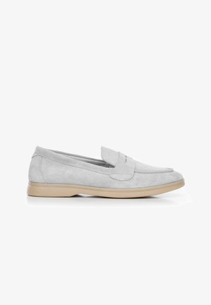 Mocassins en suède gris clair avec une semelle en caoutchouc beige plat, présentant un design classique et des accents cousus sur le dessus. Aucun matériel visible.