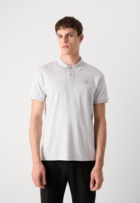 Polo cinza claro em tecido suave, com colarinho clássico, placket de três botões e um logótipo hexagonal no peito.