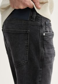 Mustad teksased, mis on kitsas lõikega, tagaküljel tasku ja nahkbrändi silt. Kangas on kergelt tekstureeritud ja nähtavate õmblustega.