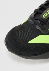 Schwarzer Sportschuh mit strukturiertem Obermaterial, ausgestattet mit neonfarbenen grünen Akzenten und einem eleganten, stromlinienförmigen Design. Die Schnürsenkel sind dunkel und ergänzen den Gesamteindruck.