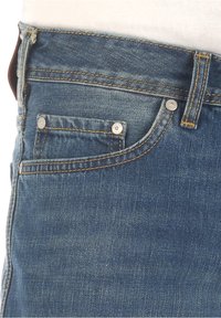 Pantalones vaqueros de mezclilla en azul oscuro con costuras visibles, que presentan un pequeño bolsillo frontal y detalles de metal en el bolsillo y la cintura.