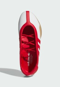 Bijela i crvena sportska cipela s tri crvena pruga, gumeni potplat i podstavljeni crveni ovratnik. Ima gornji dio od glatke kože i tonirane vezice.