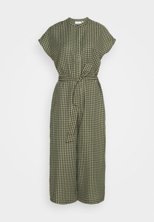 Combinaison à carreaux vert olive et noir avec manches courtes, encolure ronde, jambes larges et ceinture nouée à la taille.