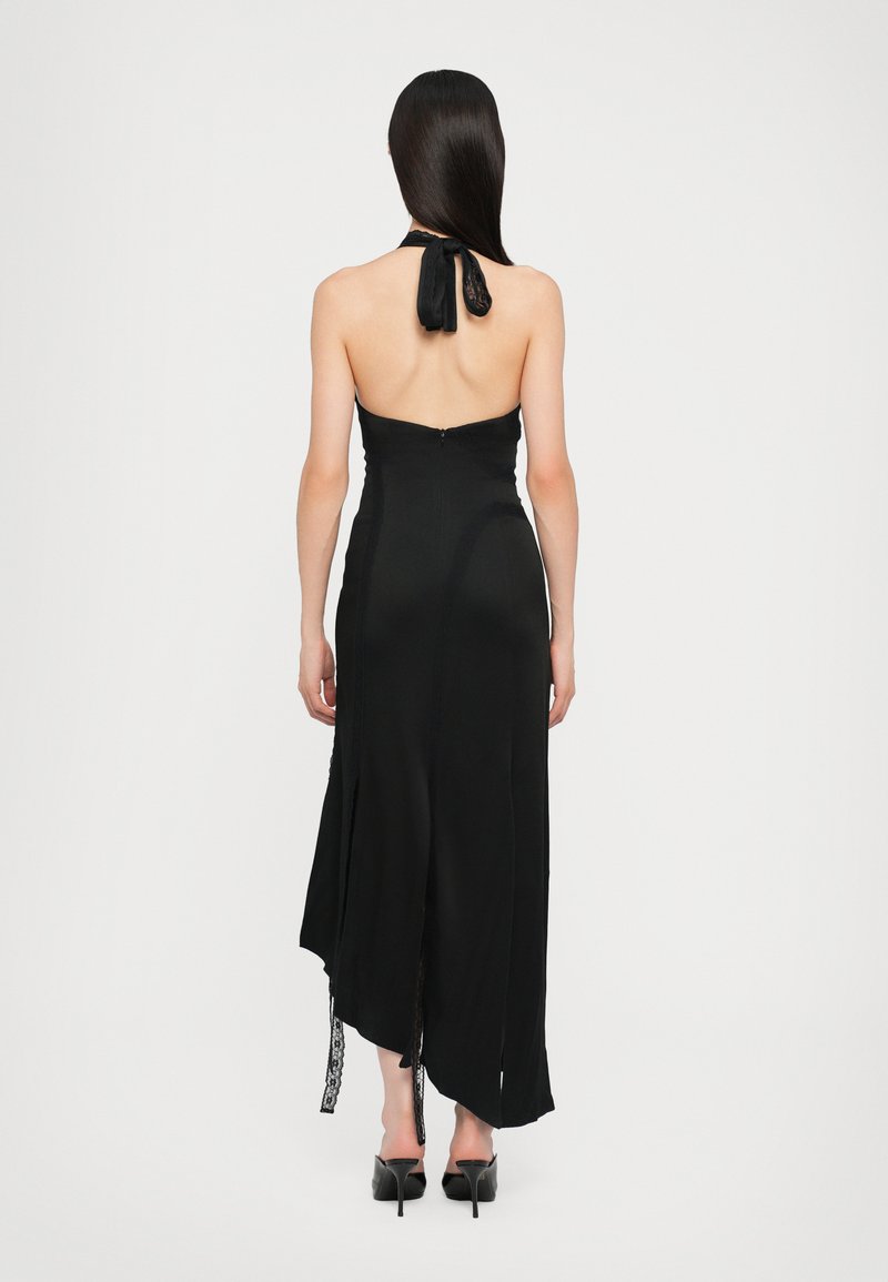 Black halter dress with a lace tie at the neck, open back, and asymmetrical hemline. Soft texture and fitted silhouette with subtle detailing.