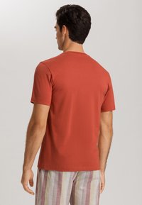 Punainen puuvillapaita, jossa on pyöreä kaula-aukko ja lyhyet hihat, yhdistettynä raidoitettuihin, vaaleanvärisiin shortseihin, joissa on pystysuoria kuvioita.