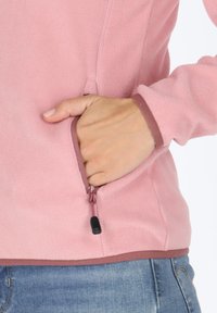 Giacca in pile rosa con tasca con zip. Presenta un bordo marrone a contrasto al colletto e all'orlo, che mette in evidenza una texture liscia.