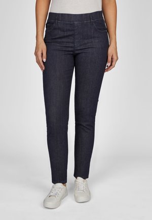 Dunkelblaue Jeans aus Denim mit schlankem Schnitt, Fünf-Taschen-Design und geradem Bein. Kombiniert mit weißen Sneakers. Leichte Textur und saubere Verarbeitung.