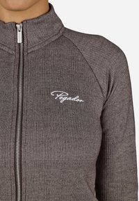 Ruda zip-up striukė, pagaminta iš raukšlėtos medžiagos, su aukštu apykakle ir baltu siuvinėtu logotipu ant krūtinės.