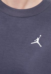 Šedé bavlnené mikina s dizajnom okrúhleho výstrihu. Obsahuje bielu vyšitú Jumpman logo na hrudi pre kontrastný akcent.