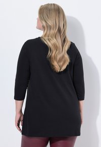 Haut noir à manches 3/4 avec un col rond, en coton doux, de longueur plus longue, associé à un pantalon bordeaux brillant.