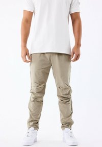 Pantalones cargo de color beige claro con bolsillos con cremallera, diseño de pierna ajustada y una textura suave. Combinados con zapatillas blancas y una camiseta blanca sencilla.