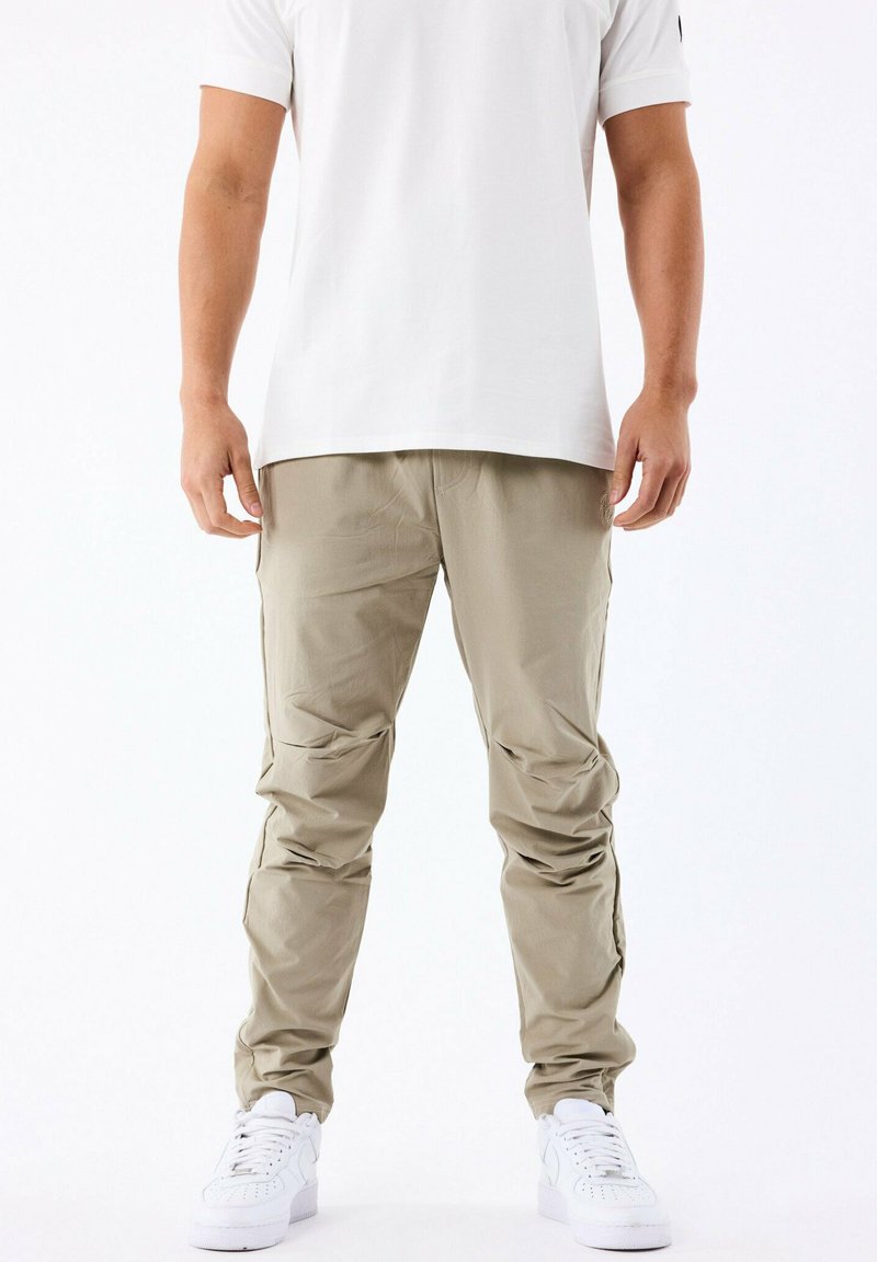 Pantalones cargo de color beige claro con bolsillos con cremallera, diseño de pierna ajustada y una textura suave. Combinados con zapatillas blancas y una camiseta blanca sencilla.