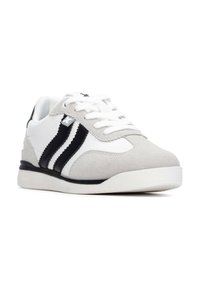 Zapatilla blanca y gris con un acabado suave de cuero y ante, que presenta franjas negras, punta redonda y cordones blancos sobre una suela texturizada.