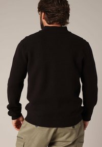 Zwarte gebreide trui met een hoge kraag, smalle mouwen en geribbelde zoom. Zachte textuur zonder zichtbare patronen of accenten.