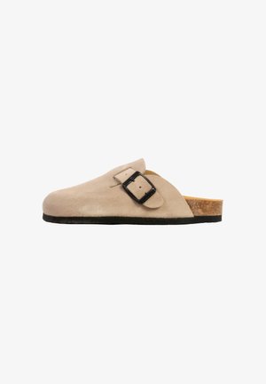 Beige ruskind slip-on træsko med sort justerbar spænde, kork-fodseng og sort sål, vist i sideprofil.