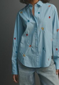 Light blue button-up shirt featuring vertical white stripes and colorful fruit embroidery. Collared with long sleeves and a relaxed fit.