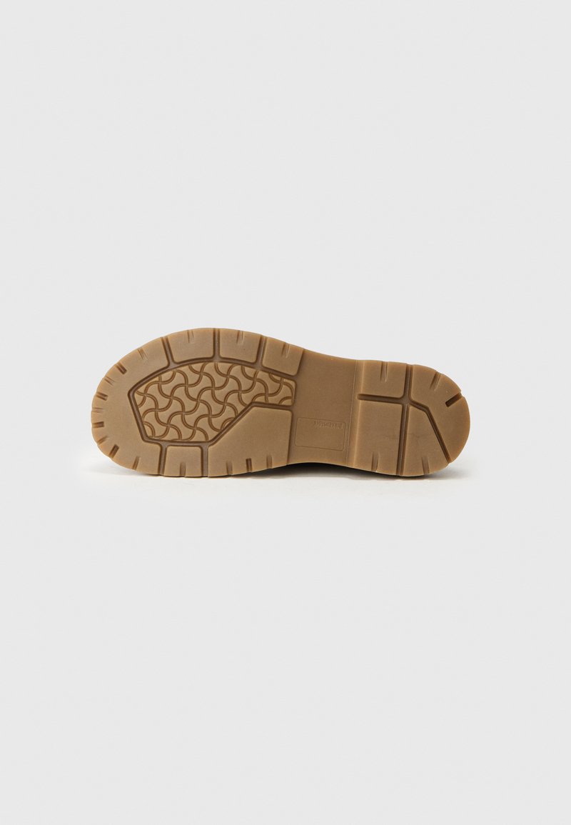 Semelle en caoutchouc de couleur brun clair avec un motif texturé. Comprend des crampons épais pour l'adhérence et la stabilité, avec des bords latéraux renforcés.