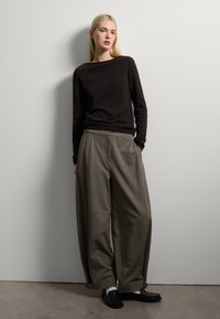 Maglione nero a maglia, pantaloni grigi larghi e scarpe nere slip-on. L'outfit presenta una vestibilità rilassata e linee semplici e pulite su uno sfondo neutro.