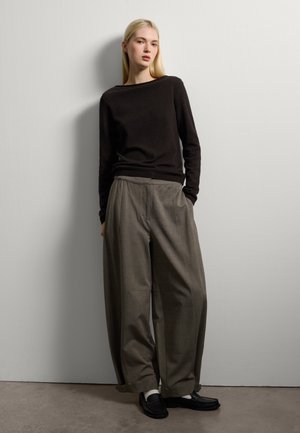Maglione nero a maglia, pantaloni grigi larghi e scarpe nere slip-on. L'outfit presenta una vestibilità rilassata e linee semplici e pulite su uno sfondo neutro.
