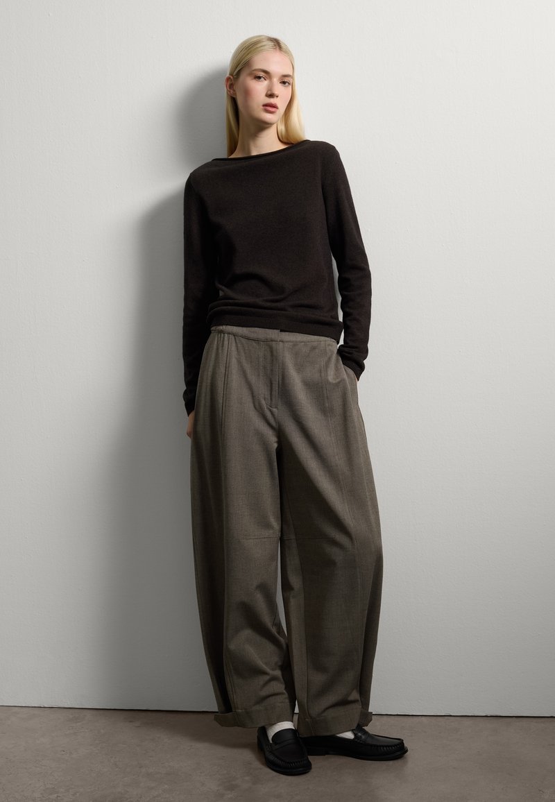 Maglione nero a maglia, pantaloni grigi larghi e scarpe nere slip-on. L'outfit presenta una vestibilità rilassata e linee semplici e pulite su uno sfondo neutro.