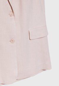 Ljust rosa, texturerat tyg med en enda ficka och två matchande knappar framtill. Rakt snitt ger en skräddarsydd look.