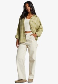 Grønternet oversized skjorte, hvid cropped tanktop, beige brede bukser, beige fodtøj. Skjorten har knaplukning og oprullede ærmer.