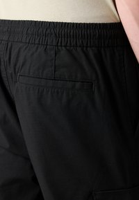 Zwarte shorts met een elastische tailleband, een gladde textuur en een achterzak met een rechthoekige flap. Eenvoudig en functioneel ontwerp.