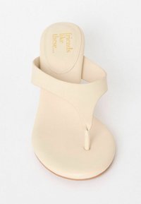 Beige flip-flop sandal med en rem mellan tårna och en slät fotbädd. Visad uppifrån med präglad text på sulan. Platt sula, minimalistisk design.