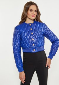 Giacca bomber in pelle trapuntata blu con bottoni dorati, polsini e orlo a costine. Presenta un collo rotondo e una texture a motivo diamante.