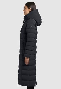 Zwarte gewatteerde lange jas met capuchon, voorzien van horizontale doorgestikte segmenten, een voorrits en een logopatch op de mouw.