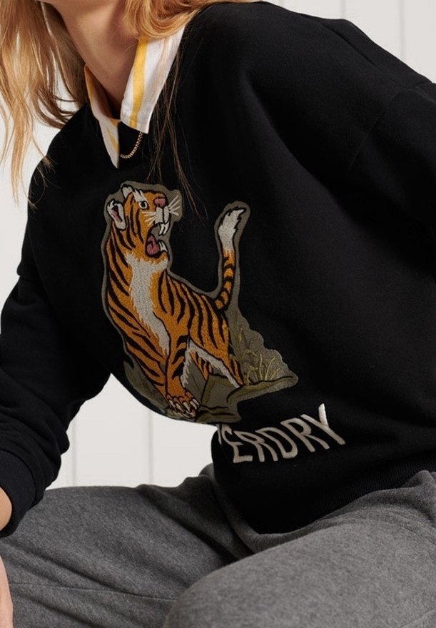 Svart sweatshirt med en stor broderad tigerdesign. Kragen har en gul och vit randig detalj. Texten "DEAD DRY" finns under tigern.