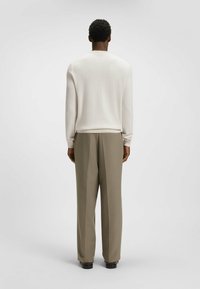 Gebreide trui in off-white met een visgraatstructuur, gecombineerd met hoogtaille rechte broek in licht kaki, gezien van achteren.