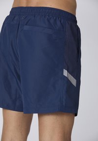 Pantaloni da bagno blu navy con vita elasticizzata, dotati di un pannello laterale in rete e un dettaglio a striscia bianca diagonale. Due tasche posteriori visibili.