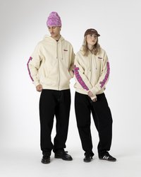 Tejdzsebb kapucnis pulóverek rózsaszín logókkal az ujjakon, fekete nadrággal párosítva. A laza megjelenést sapka és baseball sapka egészíti ki. Sima anyag.