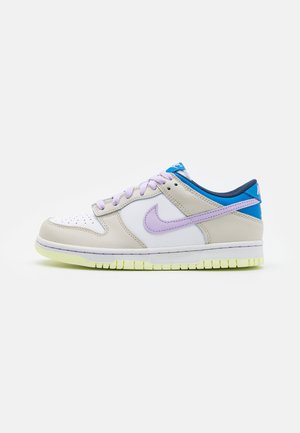 Baskets Nike avec un bout en cuir blanc, des côtés beiges, des accents violets, un talon bleu et une semelle jaune fluo. Elles possèdent des lacets ronds et un bout perforé.