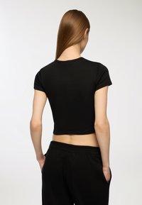 Maglietta nera a maniche corte, cropped, realizzata in un tessuto morbido. Presenta un collo rotondo e un design pulito e minimalista.